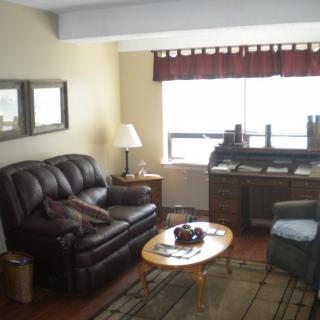 A cozy living room with a leather sofa, armchair, and a wooden desk by the window.