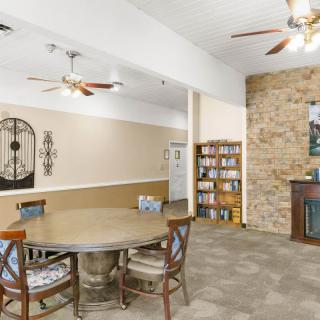 A cozy living space with a dining area, featuring a round table and chairs, a stone fireplace, and bookshelves, complemented by ceiling fans for ventilation.