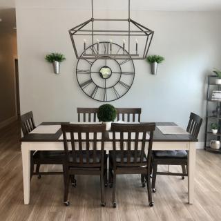 A modern dining room with a stylish dining set, geometric light fixture, and decorative wall clock.