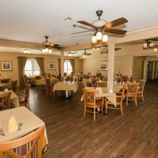 Spacious restaurant dining area with neatly arranged tables and chairs, featuring ceiling fans and a wooden floor.