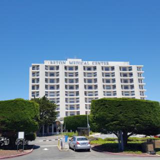 A modern hotel building under a clear blue sky, surrounded by well-manicured trees.