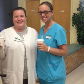 Two smiling healthcare professionals in uniforms holding beverages.