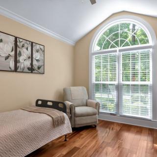 A cozy bedroom with a single bed, armchair, and a large arched window allowing natural light to fill the space.