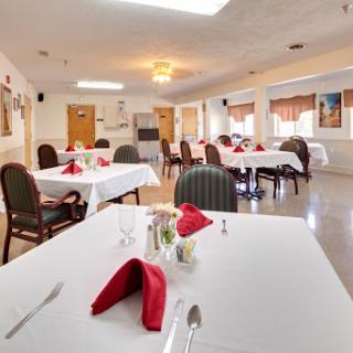 A neatly arranged dining area ready for guests, featuring tables with white tablecloths and red napkins.
