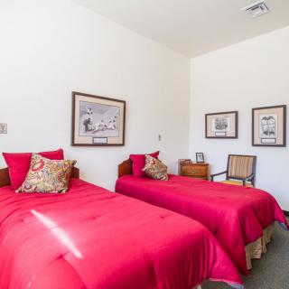 A neatly arranged bedroom featuring twin beds with vibrant red bedding and decorative pillows, complemented by framed artwork on the walls.