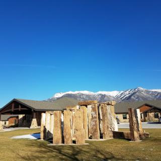 A serene landscape featuring wooden structures in the foreground, with majestic mountains and a clear blue sky in the background.