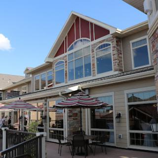 A charming restaurant featuring outdoor seating and large windows, set against a clear blue sky.
