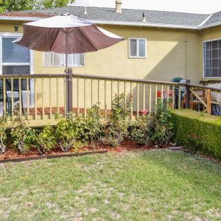 A backyard with a wooden deck, garden, and patio umbrella in front of a yellow house.