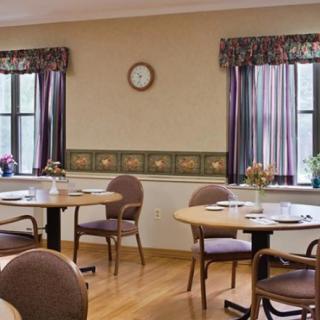 A cozy dining area with several tables and chairs, featuring patterned curtains and a wall clock.