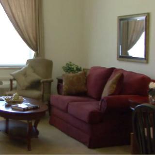 A cozy living room with a red sofa, armchair, and coffee table, complemented by curtains and a wall mirror.