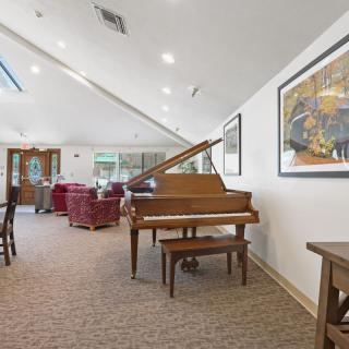 A spacious living room featuring a grand piano, comfortable seating, and artwork on the walls, illuminated by natural light from skylights.