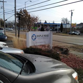 A view of a business sign from a parking lot, with cars parked in the foreground and a roadside setting.