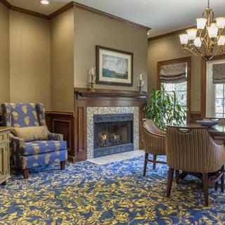 A traditionally decorated living room with a fireplace, armchair, and dining area.