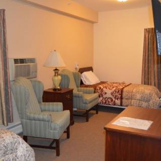 A cozy bedroom with two beds, two armchairs, a lamp on a nightstand, and a dresser.