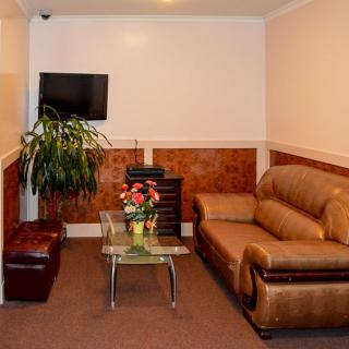 A cozy living room with a leather sofa, wall-mounted TV, indoor plant, and a glass table adorned with flowers.