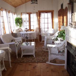 A bright and cozy sunroom featuring white wicker furniture and natural light.