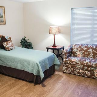A cozy bedroom featuring a single bed with a turquoise cover, a floral-patterned couch, and a lamp on a side table.