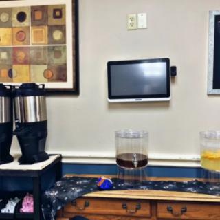 A cozy office coffee station with beverage dispensers and a digital screen.