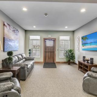 A modern waiting area featuring comfortable sofas, decorative artwork, and lush green plants.