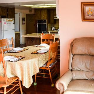 A cozy home interior featuring a dining area with a table set for four, adjacent to a kitchen and a comfortable recliner.