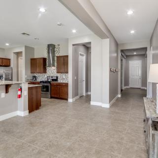 A modern kitchen and hallway area with tile flooring, wood cabinets, and recessed lighting.