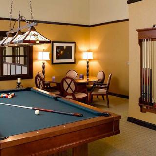 A cozy billiard room with a pool table and seating area, warmly lit by elegant lighting.