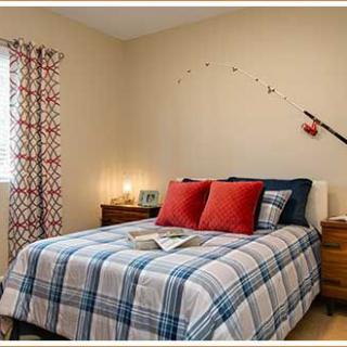 A cozy bedroom featuring a neatly made bed with plaid bedding and red accent pillows, illuminated by soft lighting from bedside lamps.