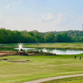 A scenic view of a golf course with a lake and fountain, surrounded by lush greenery.
