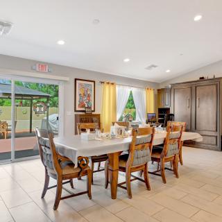A bright and spacious dining room with a large table and chairs, featuring a sliding glass door leading to the outdoors.