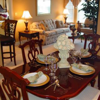 A traditional dining and living room with a polished wooden table set for dinner and cozy seating in the background.