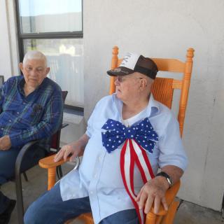 Two elderly men sitting outside, one wearing a patriotic bow tie.