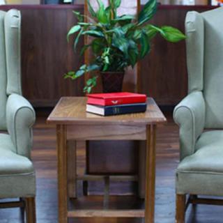 A cozy lounge area with two chairs, a wooden table, books, and a plant.