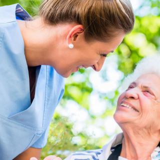 A nurse interacting compassionately with an elderly woman outdoors.