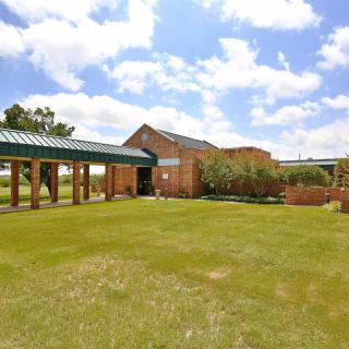 A brick building with a green roof and a spacious lawn under a partly cloudy sky.