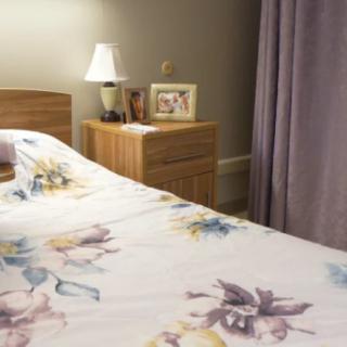 A cozy bedroom with a floral bedspread and a wooden nightstand featuring a lamp and framed photo.