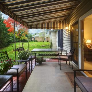A cozy backyard patio with outdoor seating under a striped canopy, surrounded by a lush garden.