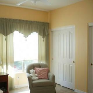 A cozy room featuring an armchair with cushions next to a window with curtains and a closet door.