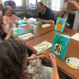 Elderly individuals participate in a group painting session, creating vibrant artwork on canvas.