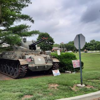 A military tank displayed in a grassy area near a stop sign.