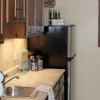 A compact kitchen with wooden cabinets, a countertop, and a black refrigerator.