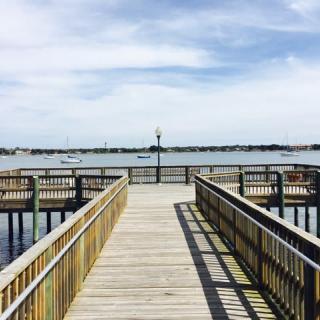 A wooden pier extending over calm water under a partly cloudy sky.