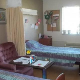 A shared hospital room with two beds separated by a curtain, featuring a window, chairs, and a small table.