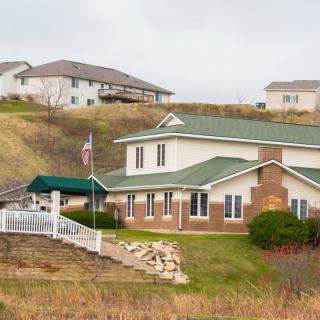 A suburban house with a green roof and a well-maintained yard, surrounded by other homes on a gentle hillside.