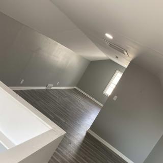 An empty room with gray walls and hardwood flooring, illuminated by natural light.