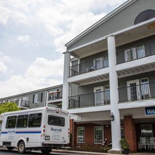 A residential building with a shuttle bus parked in front under a cloudy sky.