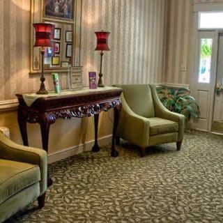 A cozy waiting area with green upholstered chairs, an ornate wooden table, and decorative red lamps.