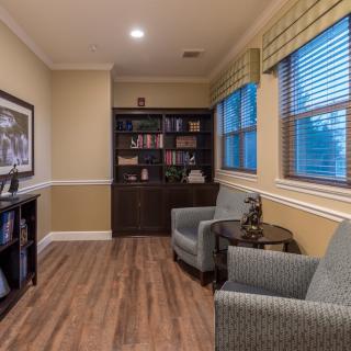 A cozy reading room with bookshelves, armchairs, and wooden flooring.