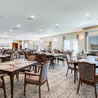 Spacious dining area with multiple tables and chairs, featuring large windows and soft lighting.
