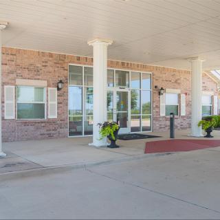 The entrance of a building with brick walls, columns, and decorative plants.