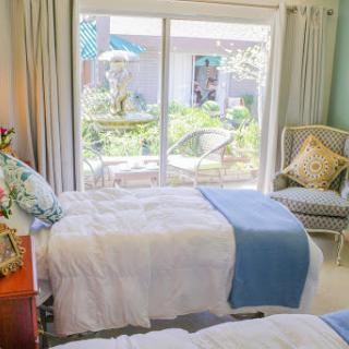 A serene and cozy bedroom featuring twin beds with soft bedding, illuminated by natural light pouring in from the garden-facing window.